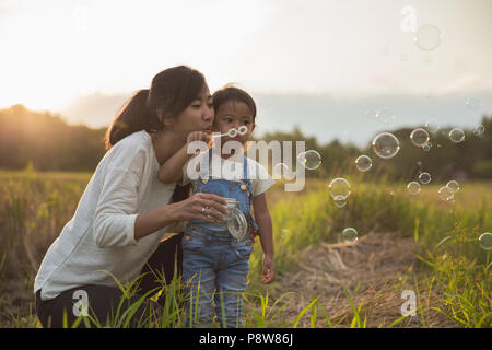 Mamma e Bambino gioca con bolla di risone di campo durante l'estate tramonto Foto Stock