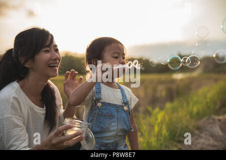 Mamma e Bambino gioca con bolla di risone di campo durante l'estate tramonto Foto Stock