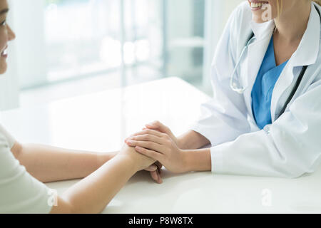 Donna Gentile Dottore mani tenendo la mano del paziente seduto alla scrivania di incoraggiamento, empatia, tifo e supporto durante la visita medica. Bad n Foto Stock