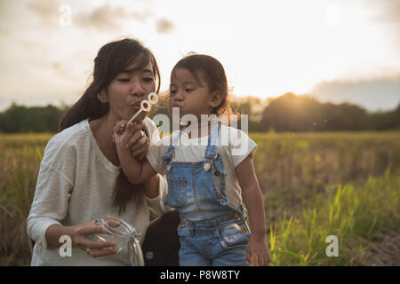 Mamma e Bambino gioca con bolla di risone di campo durante l'estate tramonto Foto Stock