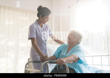 Giovani asiatici infermiera il supporto paziente anziano donna disabile in utilizzando walker in ospedale. Pazienti anziani il concetto di cura. Foto Stock