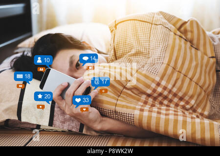 Un uomo controllare i social media e social network dopo il risveglio al mattino Foto Stock