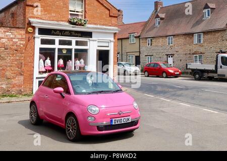 Rosa luminoso Fiat 500 davanti al grazioso e piccolo negozio di cose in Kineton, Warks. Foto Stock