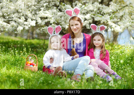 Giovane madre e le sue figlie indossando orecchie di coniglietto in un giardino di primavera nel giorno di Pasqua Foto Stock