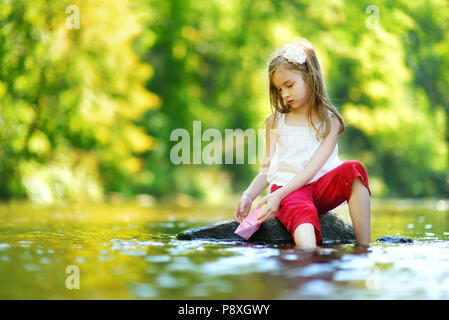 Carino bambina giocando con la barca di carta da un fiume su sole e caldo giorno d'estate Foto Stock