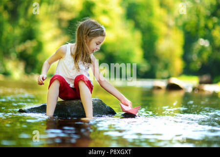 Carino bambina giocando con la barca di carta da un fiume su sole e caldo giorno d'estate Foto Stock