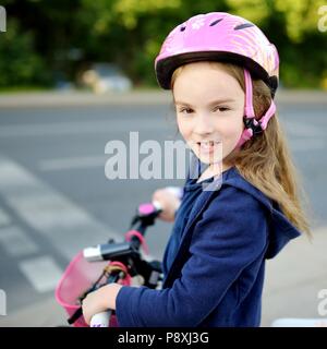 Carino piccolo preschooler ragazza in sella a una moto in una città che indossa il casco sul giorno di estate Foto Stock