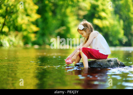 Carino bambina giocando con la barca di carta da un fiume su sole e caldo giorno d'estate Foto Stock