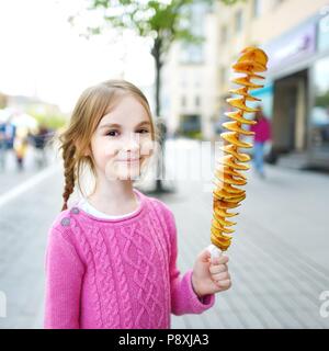 Carino bambina mangiare patate fritte su un bastone su una calda giornata estiva all'aperto Foto Stock