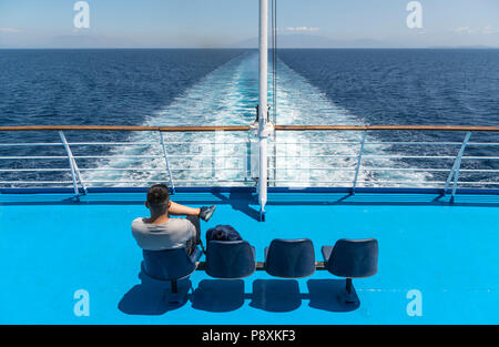 Passeggero sulla poppa di un traghetto greco a guardare la scia della nave e la terra sfuggente. Foto Stock