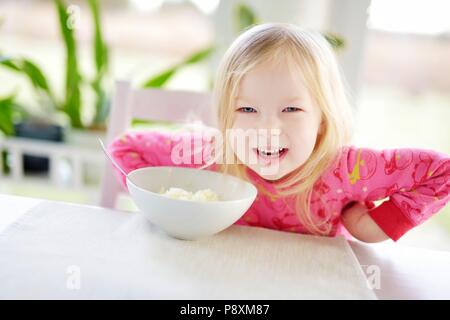 Carino bambina avente farina di avena per la colazione in cucina di sole Foto Stock