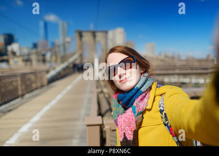 Bella giovane donna prendendo un selfie con il suo smartphone sul ponte di Brooklyn, New York, a soleggiata giornata di primavera Foto Stock