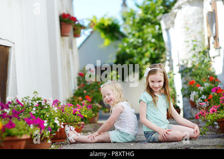 Due adorabili poco sorelle seduto tra i vasi di fiori sul sole e caldo giorno d'estate in città italiana Foto Stock