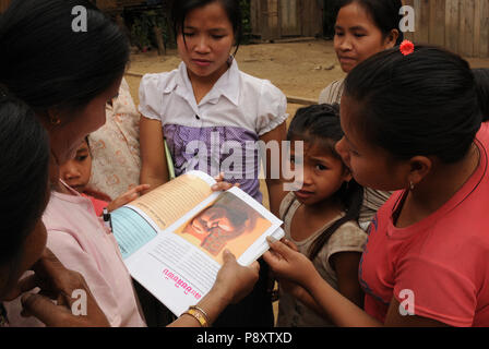 Madri e cildrens presso il divieto Huay Daue villaggio nel nord del Laos sono in cerca di nuovi libri scolastici e un referto medico. Foto Stock