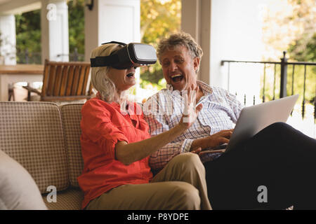 Coppia senior utilizzando laptop e sperimentando VR auricolare in veranda Foto Stock