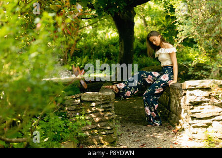 Bella donna seduta su un muro di pietra nel verde della foresta Foto Stock