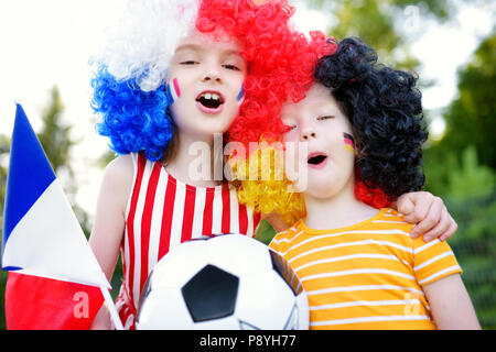 Due divertenti piccole sorelle di supporto e rasserenanti le loro squadre nazionali di calcio durante il campionato di calcio Foto Stock