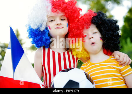 Due divertenti piccole sorelle di supporto e rasserenanti le loro squadre nazionali di calcio durante il campionato di calcio Foto Stock