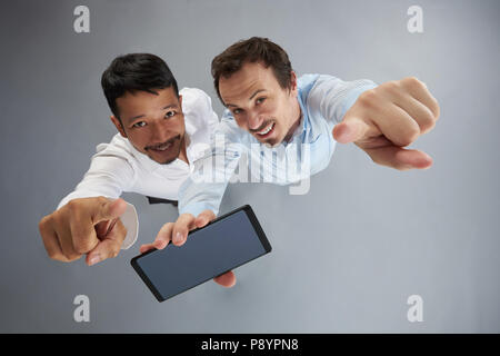 Due sorridente mans tenendo lo smartphone e punto con dita isolato su sfondo grigio sopra vista superiore Foto Stock