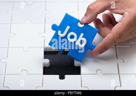 La mano di una persona immissione finale pezzo blu con processo in parola puzzle Foto Stock