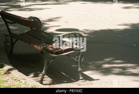 Giardino Vintage Panca con struttura in metallo e legno posti su asfalto park alley nella struttura ad albero ombra nella soleggiata giornata estiva Foto Stock