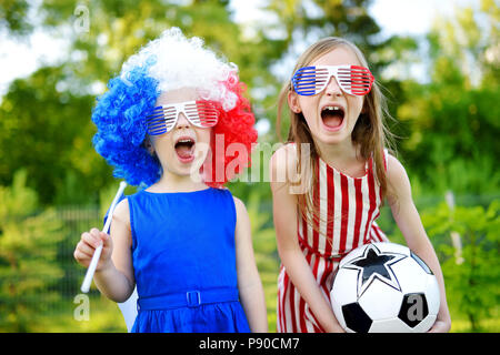 Due divertenti piccole sorelle di supporto e il tifo la loro squadra nazionale di calcio durante il campionato di calcio Foto Stock