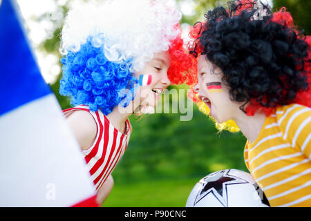 Due divertenti piccole sorelle di supporto e rasserenanti le loro squadre nazionali di calcio durante il campionato di calcio Foto Stock