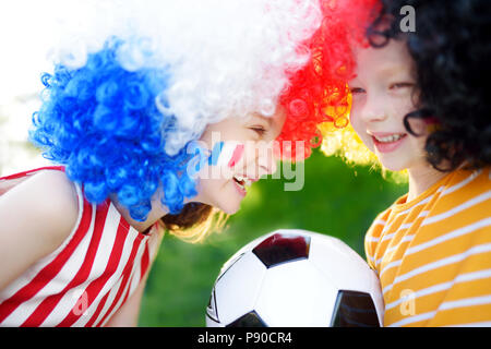 Due divertenti piccole sorelle di supporto e rasserenanti le loro squadre nazionali di calcio durante il campionato di calcio Foto Stock