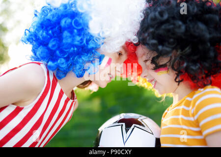 Due divertenti piccole sorelle di supporto e rasserenanti le loro squadre nazionali di calcio durante il campionato di calcio Foto Stock