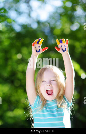 Adorabile bambina con le sue mani dipinte di divertimento all'aperto sulla luminosa giornata estiva Foto Stock