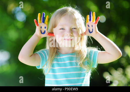 Adorabile bambina con le sue mani dipinte di divertimento all'aperto sulla luminosa giornata estiva Foto Stock