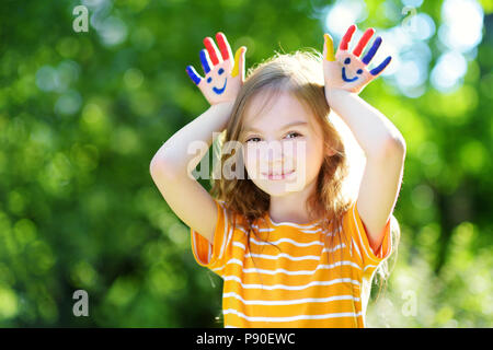 Adorabile bambina con le sue mani dipinte di divertimento all'aperto sulla luminosa giornata estiva Foto Stock