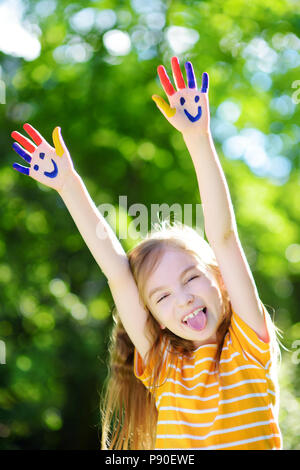 Adorabile bambina con le sue mani dipinte di divertimento all'aperto sulla luminosa giornata estiva Foto Stock