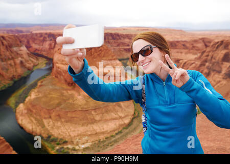 Giovane turista di scattare una foto di se stessa dalla famosa curva a ferro di cavallo, Arizona, Stati Uniti d'America Foto Stock