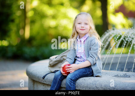 Adorable Little Schoolgirl in un parco della città sulla luminosa giornata autunnale Foto Stock