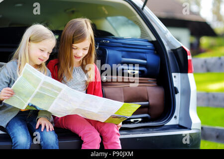 Due adorabili poco sorelle ad esplorare una mappa prima di andare in vacanza con i loro genitori. Due bambini di guardare avanti per un viaggio su strada o in viaggio. Foto Stock