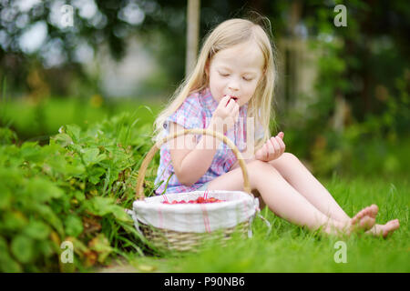 Carino bambina picking fresche fragole selvatiche su organic strawberry farm su sole e caldo giorno d'estate Foto Stock