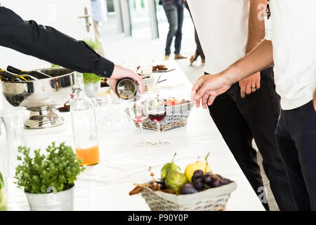 Cameriere versando il vino rosso di vetro per due uomini di colore bianco sul Tavolo da Buffet Foto Stock