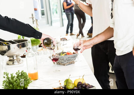 Cameriere versando il vino rosso di vetro per due uomini di colore bianco sul Tavolo da Buffet Foto Stock