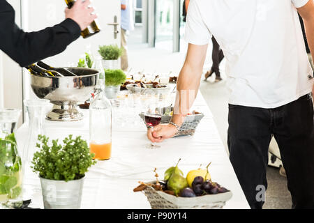 Cameriere versando il vino rosso di vetro per due uomini di colore bianco sul Tavolo da Buffet Foto Stock