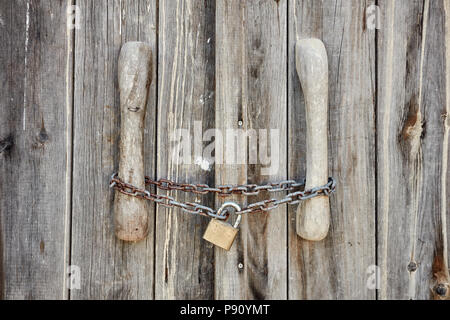 Vista ravvicinata di una vecchia porta di legno bloccato con rusty catena e lucchetto Foto Stock