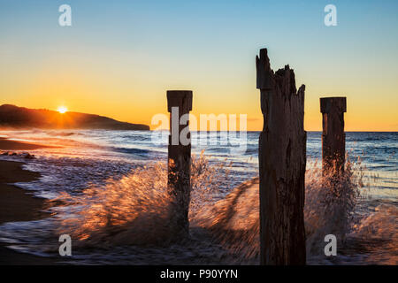 Spruzzi delle onde contro il vecchio molo posti su St Clair beach, Dunedin, Otago, come il sole sorge. Foto Stock