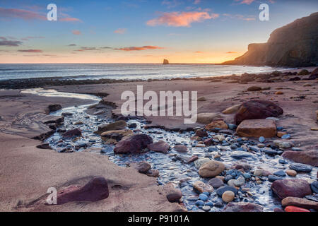 La spiaggia di Saltwick Bay, North Yorkshire, Inghilterra, Regno Unito, a sunrise. La pila del mare è noto come nero Nab. Foto Stock