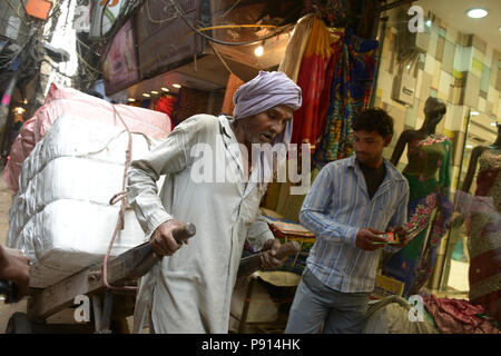 Indian uomo tira un rickshaw carrello in strada trafficata strada di Delhi città vecchia, fotografati da un tuc tuc ride Foto Stock