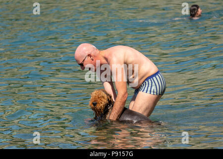 Strunjan, Slovenia, 14 luglio 2018. Un uomo si aggiorna il suo cane in un mare adriatico spiaggia in Strunjan riserva naturale, che è la sezione più lunga di u Foto Stock