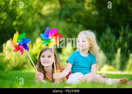 Due graziosi bambine holding colorato pinwheels giocattolo sul sole e caldo giorno d'estate Foto Stock