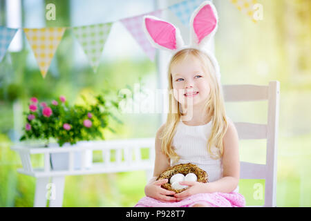 Carino bambina indossa orecchie di coniglietto giocando caccia all'uovo di Pasqua. Adorabile bambino celebrare la Pasqua in casa. Foto Stock