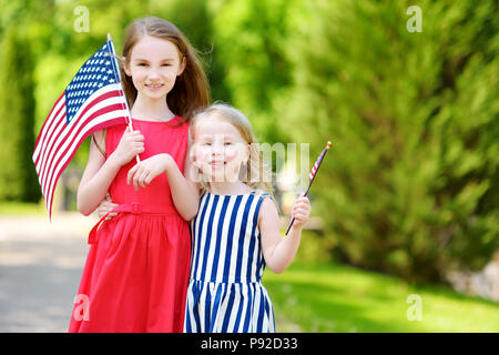 Due adorabili poco sorelle tenendo bandierine americane all'aperto nella bella giornata d'estate. Giorno di indipendenza del concetto. Foto Stock