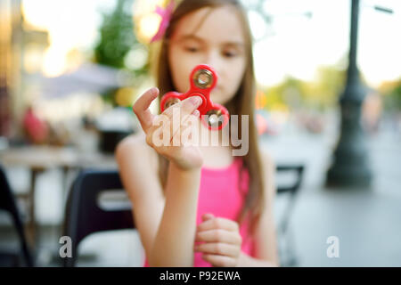 Scuola carina ragazza che gioca con colorati agitano: spinner in outdoor cafe. Popolari antistress giocattolo scuola per bambini e adulti. Foto Stock