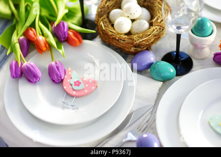 Bella tavola apparecchiata con stoviglie e fiori per la festa di Pasqua. Bicchieri e posate per catering cena evento. Foto Stock
